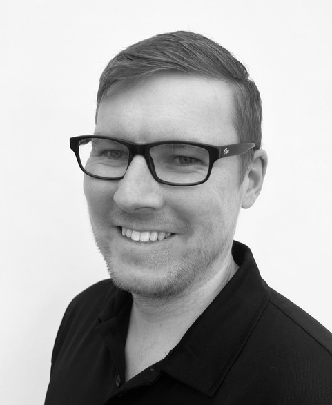 A black and white headshot of ben smiling at the camera.