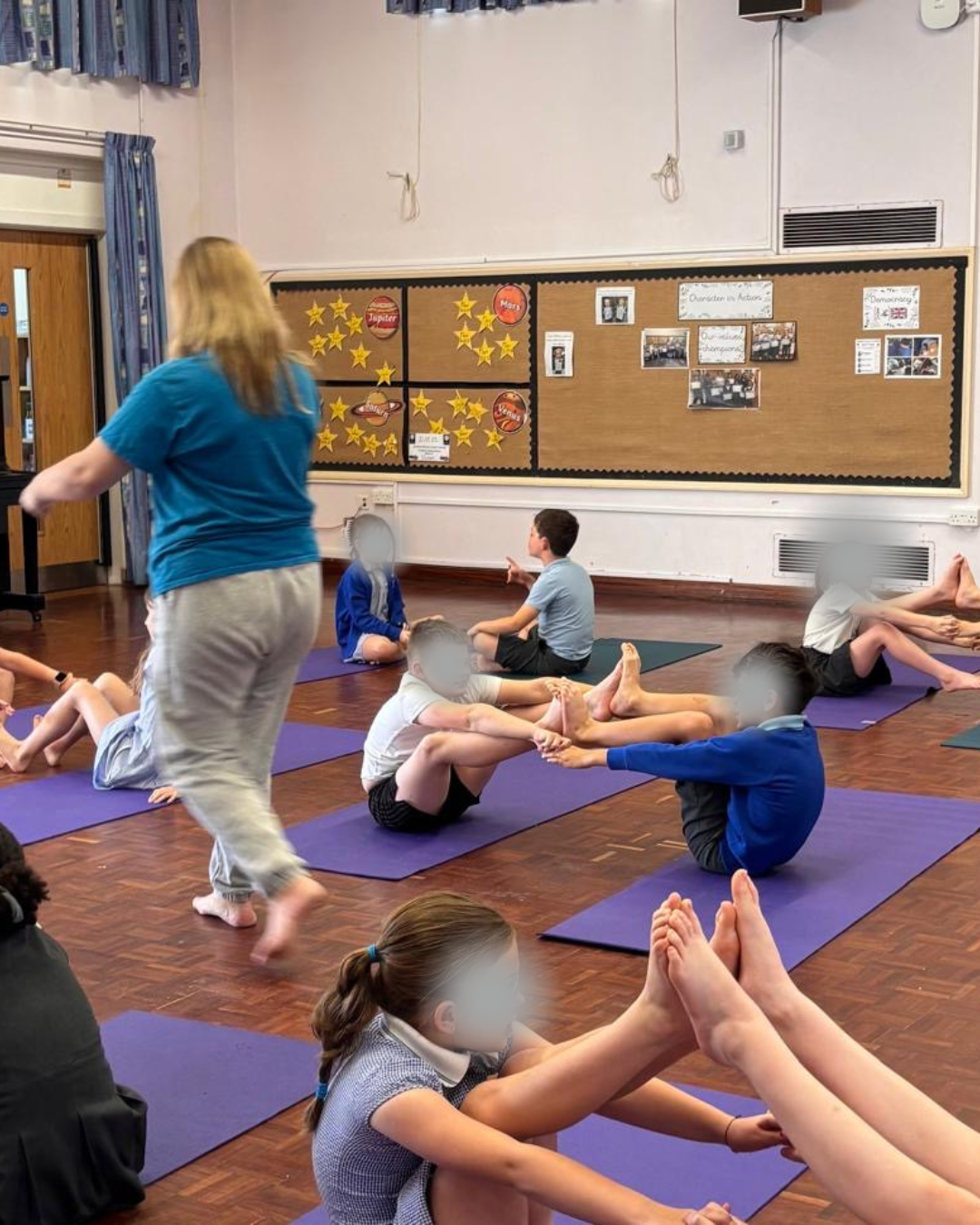Participants doing yoga boat pose in a school hall